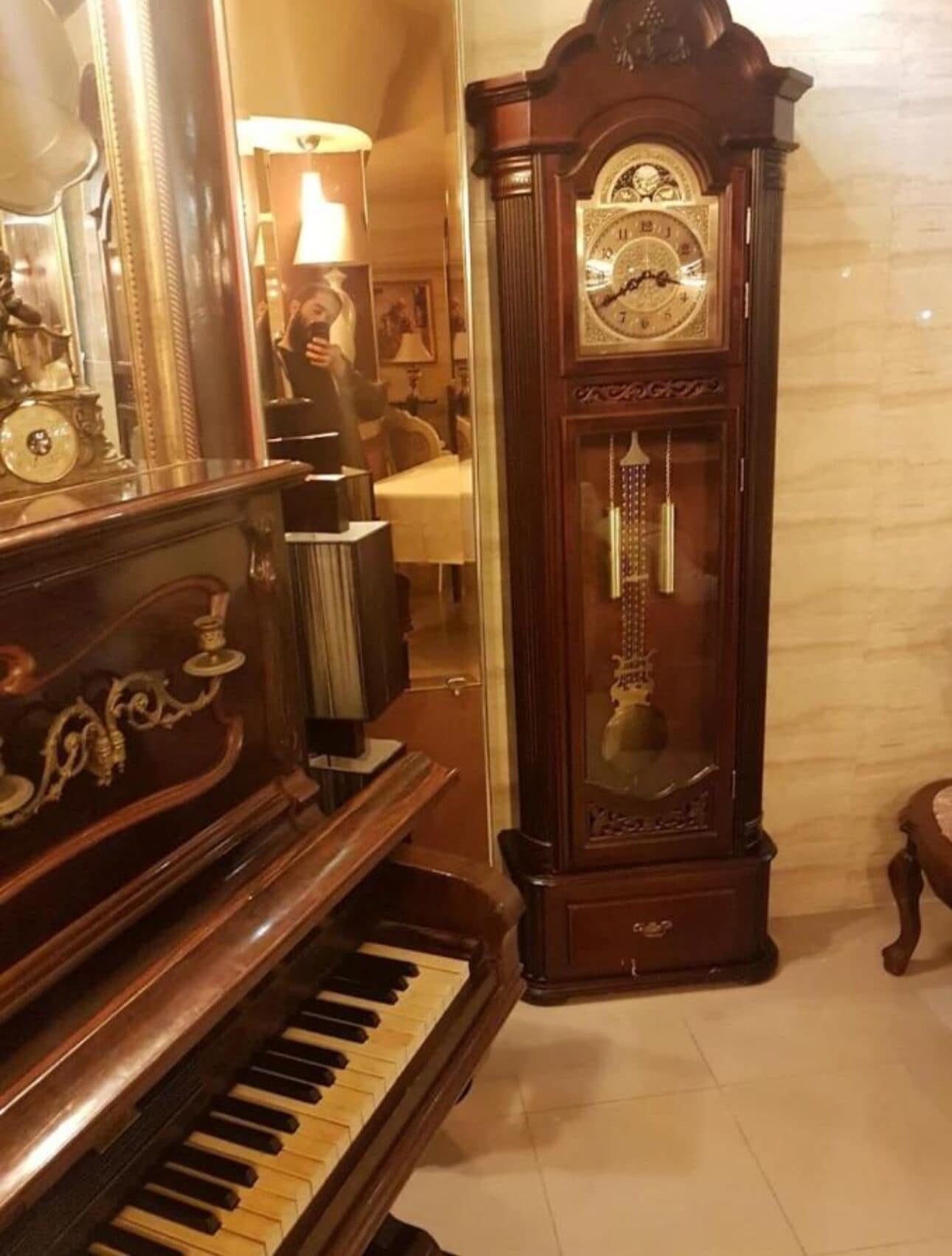 Um piano de cauda imponente e um relógio de chão alto e ricamente decorado em um quarto com iluminação acolhedora e piso de mármore.