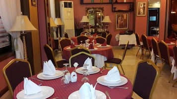 A dining area with round tables set for four, each with white plates, folded napkins, and cutlery.