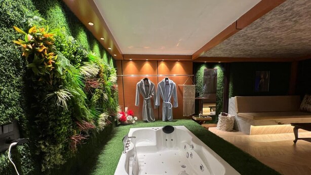 A modern bathroom with a large jacuzzi tub, green artificial grass, and a wall of lush plants. - Desire Stay (New Delhi)