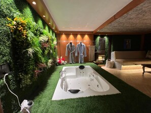 A modern bathroom with a large jacuzzi tub, green artificial grass, and a wall of lush plants. - Desire Stay (New Delhi)