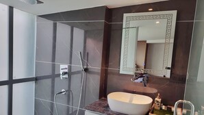 A modern bathroom with a glass shower enclosure, a freestanding bathtub, and a vanity with a marble countertop. - Desire Stay (New Delhi)