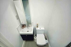 A small bathroom with a sink, mirror, toilet, and a small cabinet. - Charming Studio 30min to Central London (Wembley)