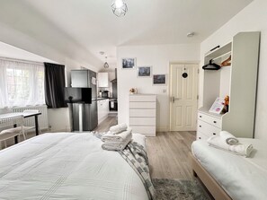 A modern hotel room with a bed, a desk, a kitchenette, and a wardrobe. - Charming Studio 30min to Central London (Wembley)