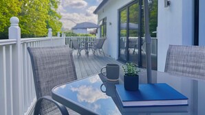 Een glazen tafel met een boek en een mok er op, onder een zonnescherm.