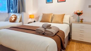 A hotel room with a neatly made bed, a bedside table with a lamp, and two framed artworks on the wall. - Family-Friendly En-suite 30min to Central London (Wembley)