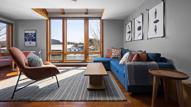 A modern living room with a sofa, armchair, coffee table, and artwork on the wall.