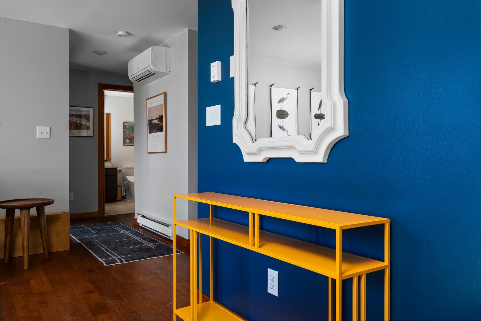 A hallway with a blue wall, a yellow console table, and a white decorative mirror.