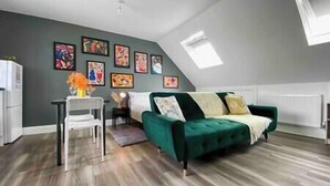 A modern loft-style living room with a green sofa, a dining table with chairs, and a variety of colorful artwork on the walls. - Bright Studio Loft 30min to Central London (Wembley)