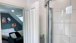 A room with a glass shower door, a white door, and a view into a living area with a sofa and artwork on the wall. - Bright Studio Loft 30min to Central London (Wembley)