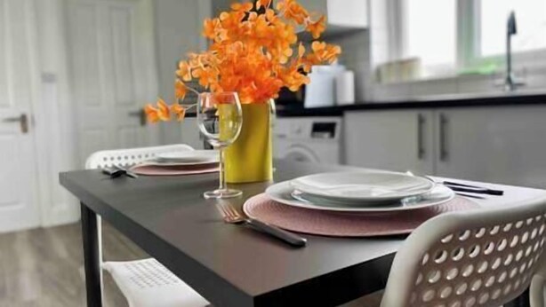 A dining table set with plates, a glass, and a vase of orange flowers. - Bright Studio Loft 30min to Central London (Wembley)