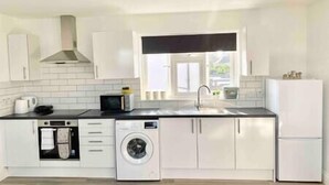 A modern kitchen with white cabinetry, a built-in oven, a washing machine, and a sink. - Bright Studio Loft 30min to Central London (Wembley)