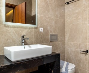 A bathroom with a white sink, black countertop, and beige marble tiles. - The Owl House - Studio #1 (Chania)