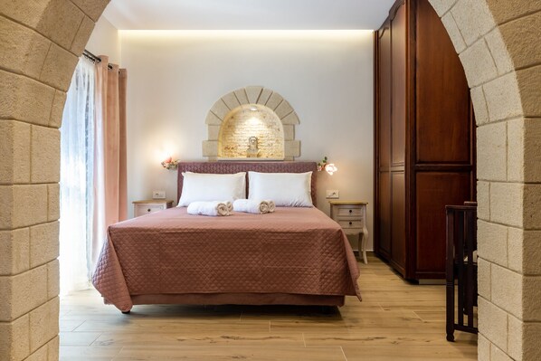 A bedroom with a large bed, a stone arch wall, and a wooden wardrobe. - The Owl House - Studio #1 (Chania)