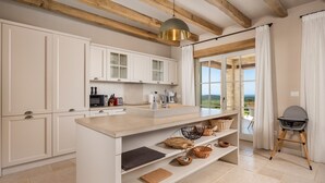 Une cuisine avec des armoires blanches, un grand îlot central et une vue sur l’extérieur.