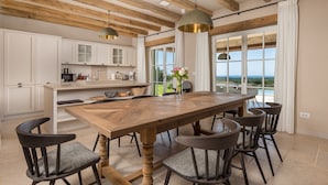 Une cuisine spacieuse avec des poutres en bois, des armoires blanches et une grande table à manger avec des chaises.