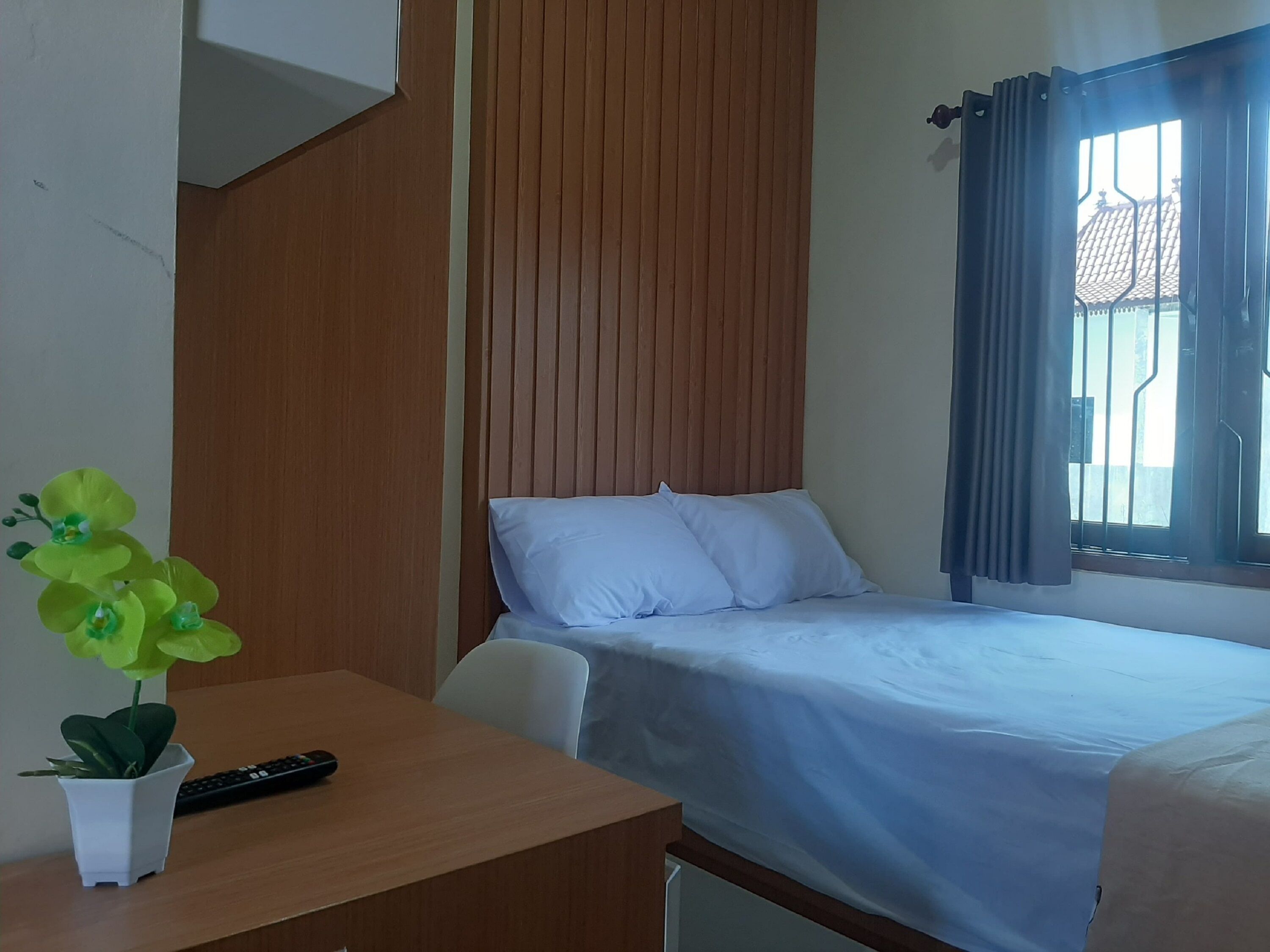 Una camera d'albergo con un letto, una scrivania con un telecomando e una pianta in vaso.