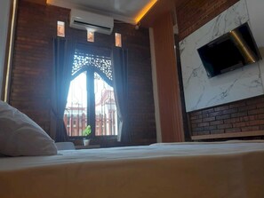 A hotel room with a bed, a TV mounted on the wall, a window with a decorative screen, and an air conditioning unit. - Capital O 93719 Homestay Omah Bidadari (Prambanan)