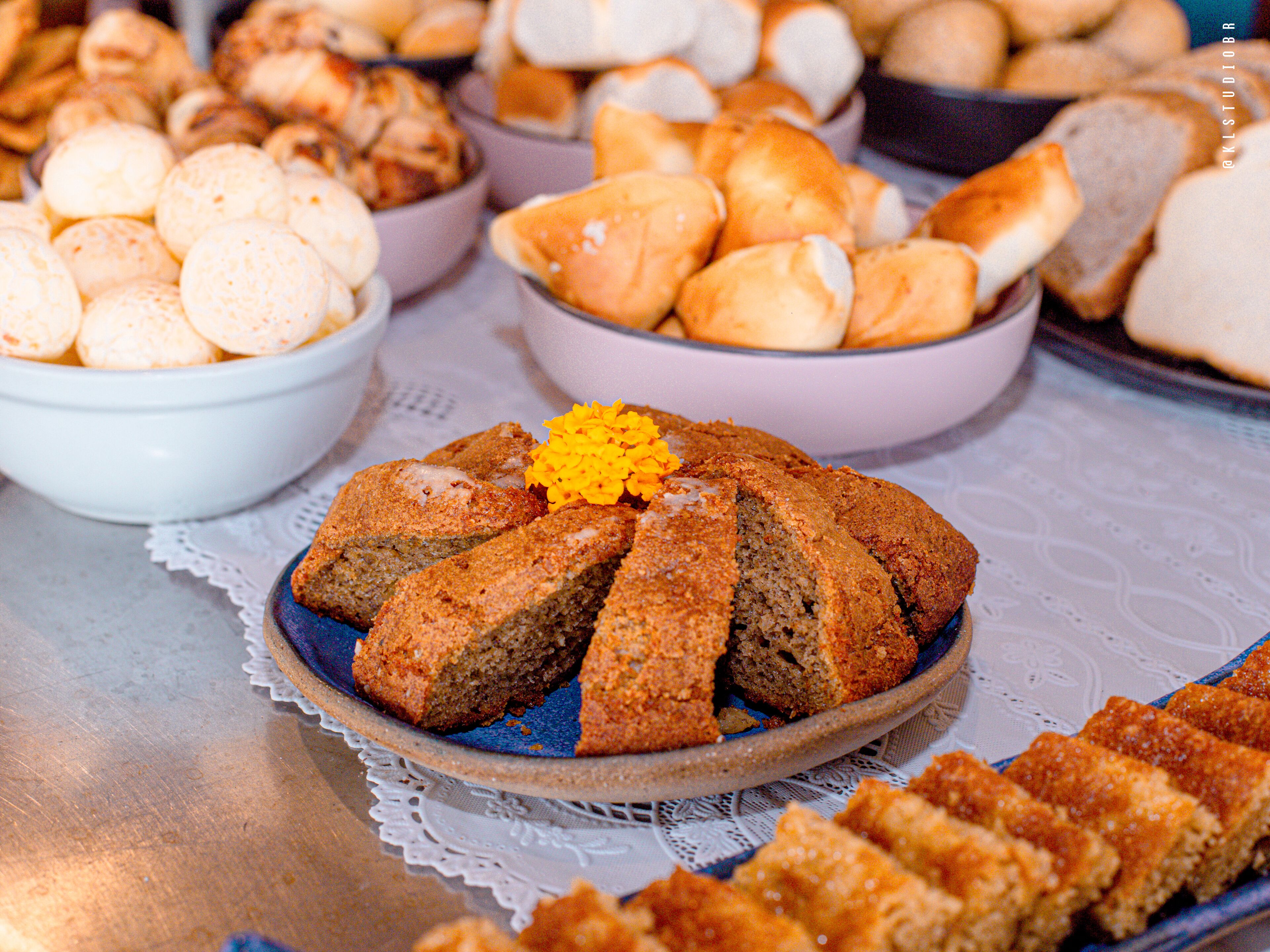 Une table où sont présentés divers produits de boulangerie, notamment un gâteau décoré d’une fleur jaune, des petits pains et d’autres pâtisseries.