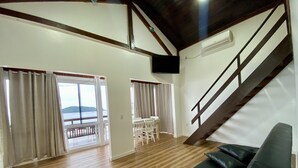 Uma sala de estar ampla com piso de madeira, um sofá preto, uma mesa de jantar com cadeiras e uma escada.