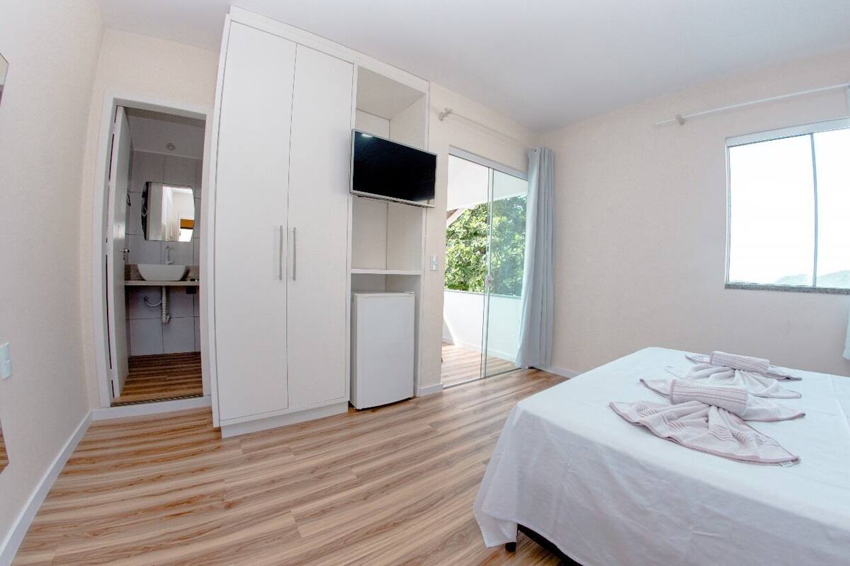 A bedroom with a bed, a TV, a wardrobe, and a balcony.