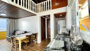 Uma área de refeições com mesa e cadeiras, uma cozinha com geladeira e pia, e uma varanda com guarda-corpo.