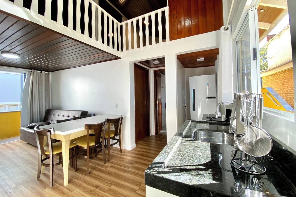 A dining area with a table and chairs, a kitchen with a refrigerator and sink, and a balcony with a railing.