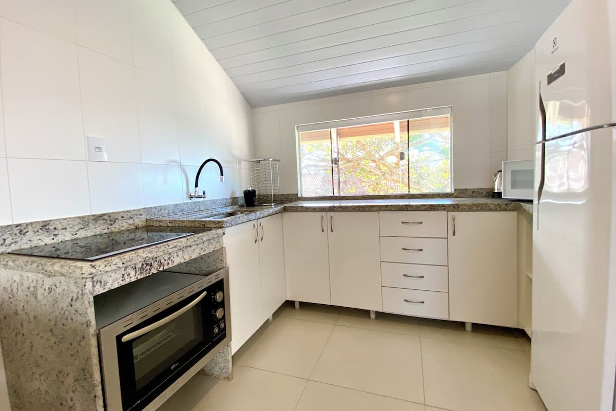 A kitchen with white cabinets, a granite countertop, a built-in oven, a microwave, and a window with a view of trees.