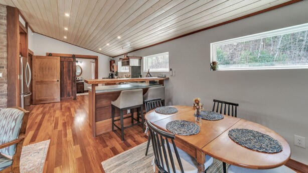 A spacious kitchen with a wooden ceiling, a dining area with a large table and chairs, and a view of the outdoors through a window.