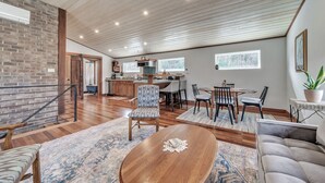 A spacious living area with a wooden ceiling, a dining table with chairs, a sofa, and a kitchen in the background.