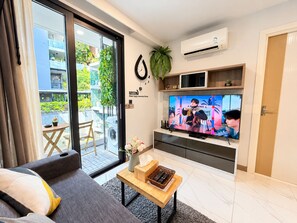 A modern living room with a sofa, a coffee table, a flat-screen TV, and a sliding glass door leading to an outdoor balcony.