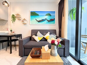 A modern living room with a grey sofa, a coffee table, a painting of boats on water, and a window with curtains.