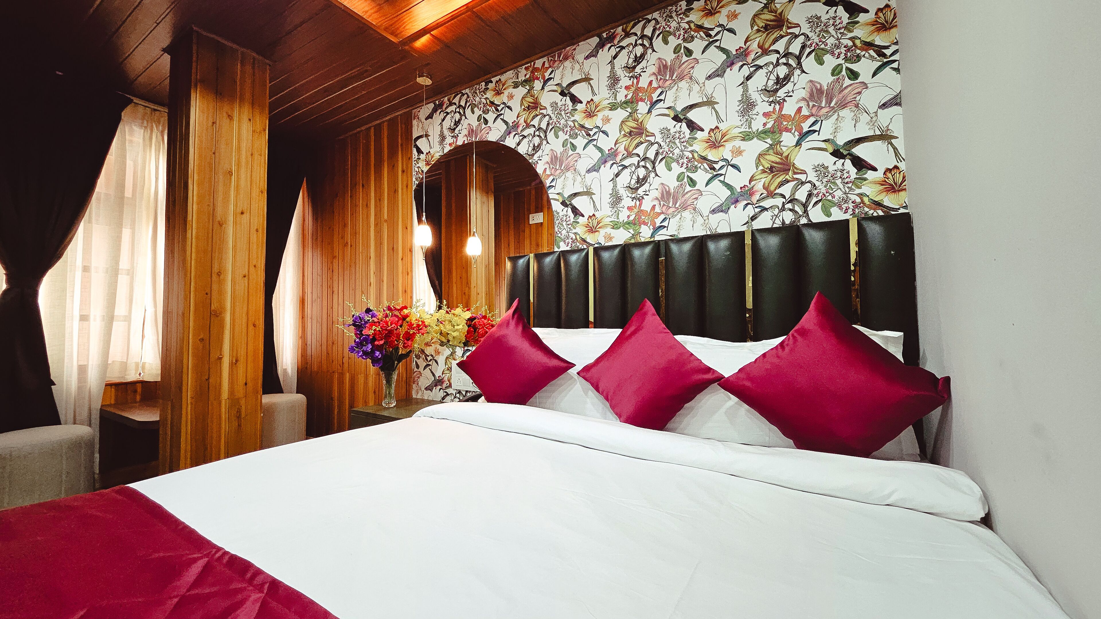 Ein Hotelzimmer mit einem hölzernen Kopfteil, einem Bett mit weißer und roter Bettwäsche und floralem Wandpapier.