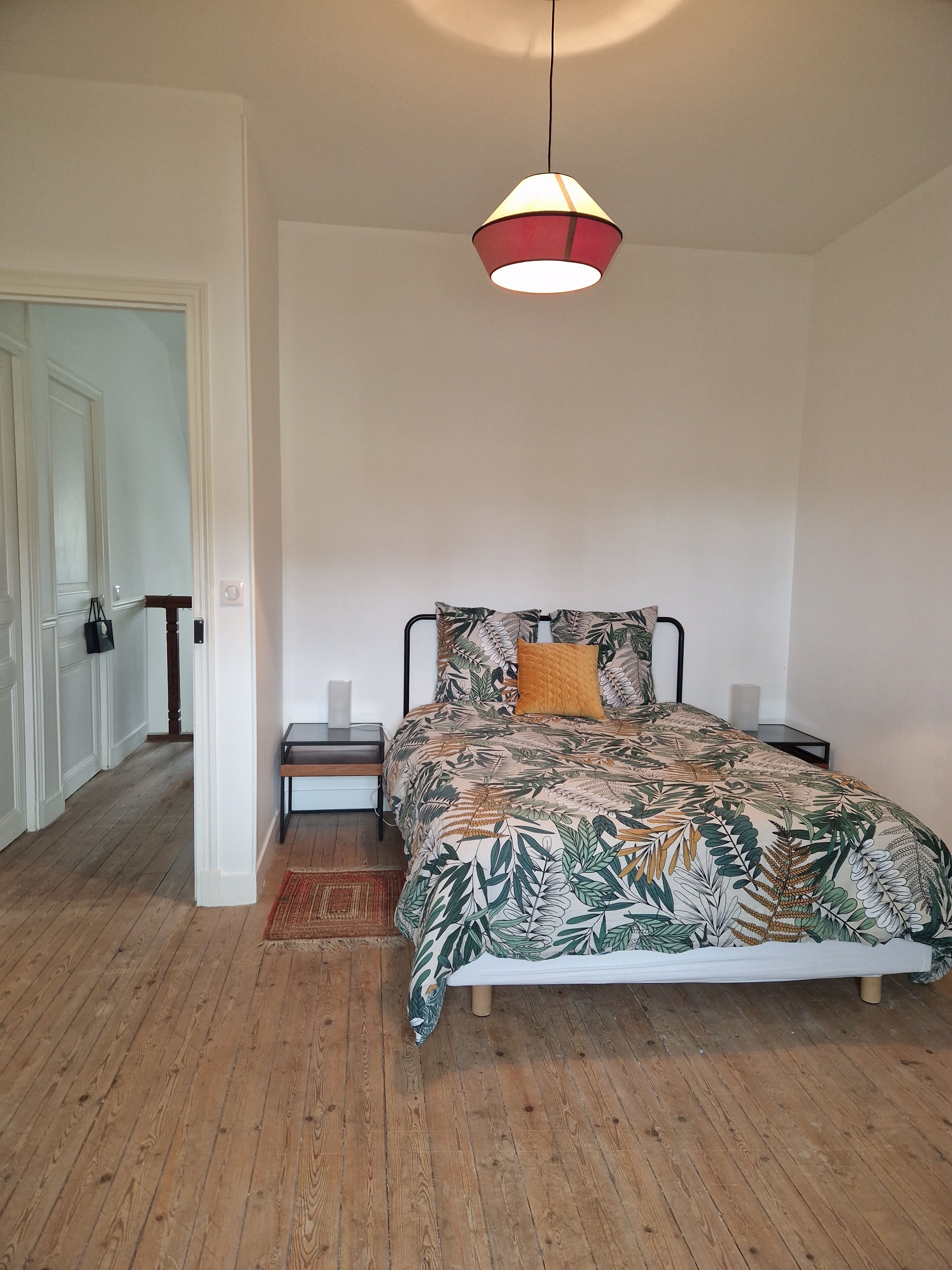 A bedroom with a bed, a nightstand, a lamp, and a hanging light fixture.