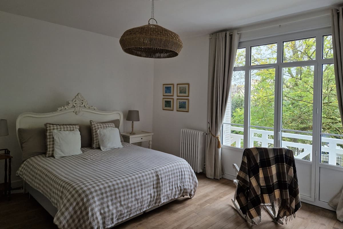 A bedroom with a large bed, a bedside table with a lamp, a radiator, and a window with curtains.