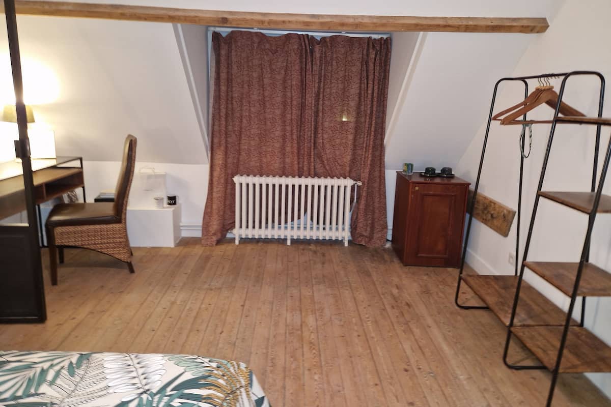 A room with a sloped ceiling, a radiator, a chair, a desk, a hanging rack, and a bed.