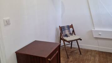 Una habitación con piso de madera, un mueble pequeño de madera, una silla con una manta de cuadros y un sombrero colgado en la pared.