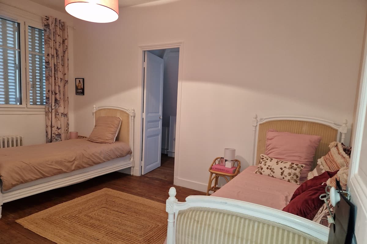 A bedroom with two single beds, a wooden floor, a woven rug, and a door leading to another room.