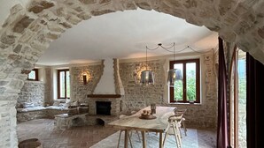 Un intérieur rustique avec des murs en pierre, une cheminée en pierre, des meubles en bois et de grandes fenêtres.