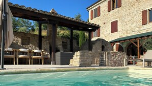 Un espace piscine agrémenté de murs en pierre, de sièges extérieurs et d’un patio couvert.