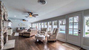 A spacious living room with a fireplace, large windows, and a ceiling fan. - Coastal Oasis - Beautiful Ocean Views Awaits (Corpus Christi)