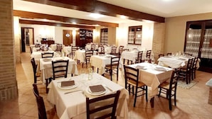 A spacious dining area with multiple tables set for dining, featuring a brick wall and wooden beams on the ceiling. - LOCANDA DEL VIANDANTE (Magliano Alfieri)