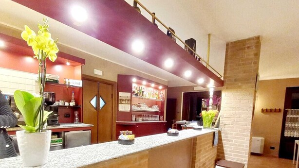 A reception area with a counter, a potted plant, a bar area with bottles, and a staircase. - LOCANDA DEL VIANDANTE (Magliano Alfieri)