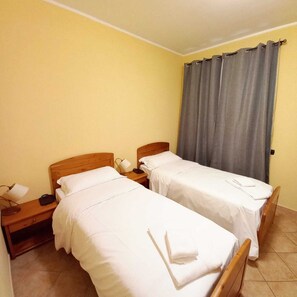 A hotel room with two single beds, wooden headboards, white linens, a nightstand with a lamp, and a window with grey curtains. - LOCANDA DEL VIANDANTE (Magliano Alfieri)