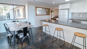 Une cuisine moderne avec un coin repas, comprenant une table avec des chaises, un comptoir-bar avec des tabourets et un ventilateur de plafond.