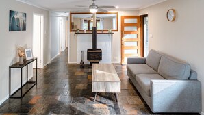 Un salon spacieux doté d’un sol en pierre, d’un canapé gris, d’une table basse en bois, d’une cheminée et d’un ventilateur de plafond.