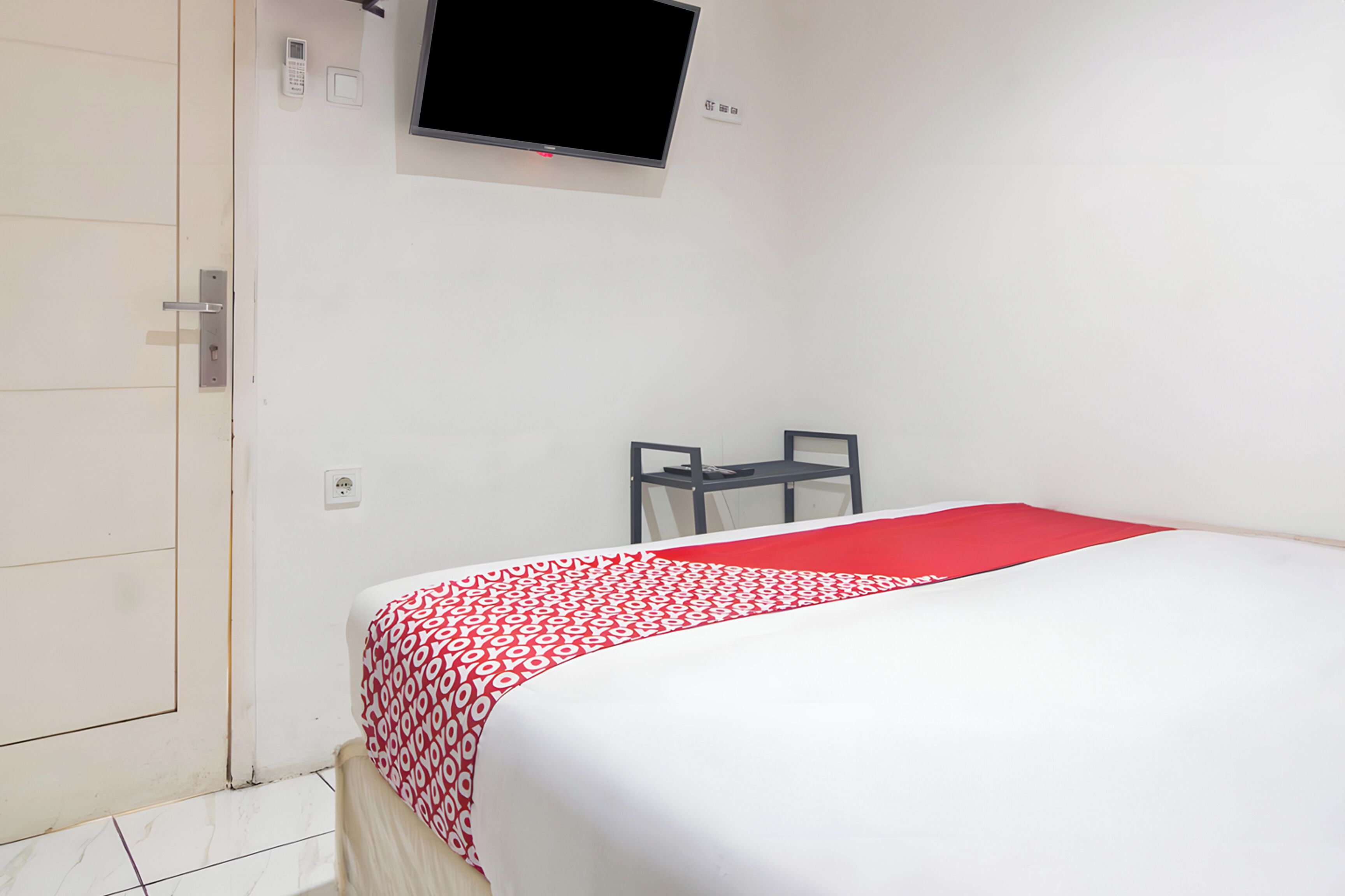 Una habitación de hotel con cama, televisor montado en la pared, escritorio y silla.