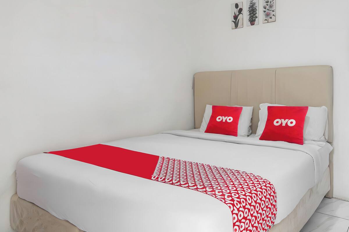 A bed with a white and red bedspread, two red pillows with "OYO" branding, and a beige headboard.