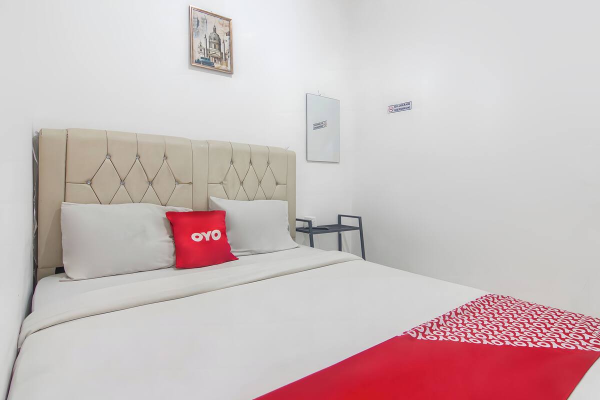 A hotel room with a bed, a red and white patterned throw, and a headboard with a diamond pattern.