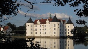 Un bâtiment qui ressemble à un château, doté de nombreuses tours et entouré d’eau et d’arbres.
