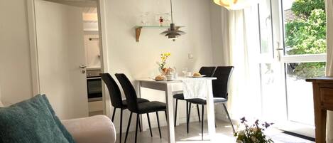 Ein modernes Wohnzimmer mit einer Couch, einem Esstisch mit Stühlen und einer Küche im Hintergrund.